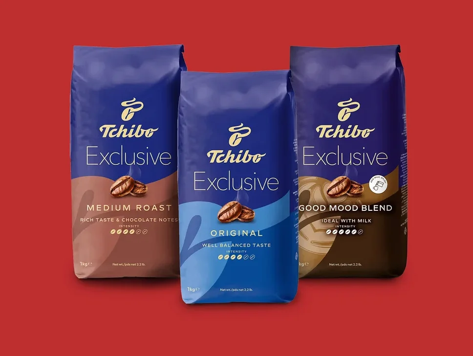 Három kék Tchibo Exclusive kávécsomag áll piros háttér előtt. Balról jobbra: Medium Roast barna aljjal, Original világoskék aljjal és Good Mood Blend sötétbarna aljjal.