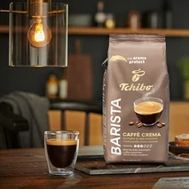 Egy csomag BARISTA Caffè Crema - 1x1 kg szemes kávé egy asztalon áll egy pohár kávé mellett.