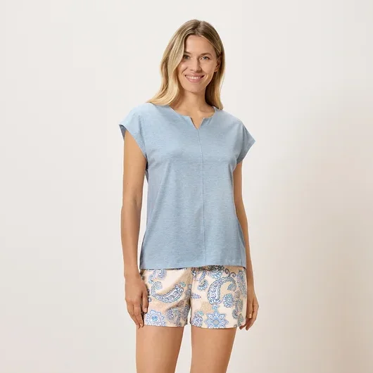 Eine Frau steht und trägt ein blaues T-Shirt und gemusterte Shorts.