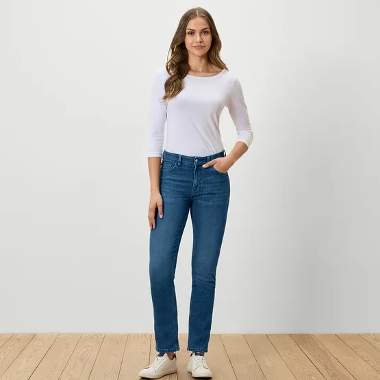 Frau steht und posiert in blauen Jeans, weißem T-Shirt und weißen Turnschuhen.