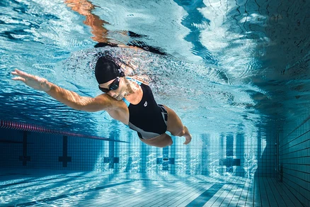 Nő úszik a medencében a víz alatt, fekete arena Feel Lily Swim Pro Back Bustier fürdőruhában.