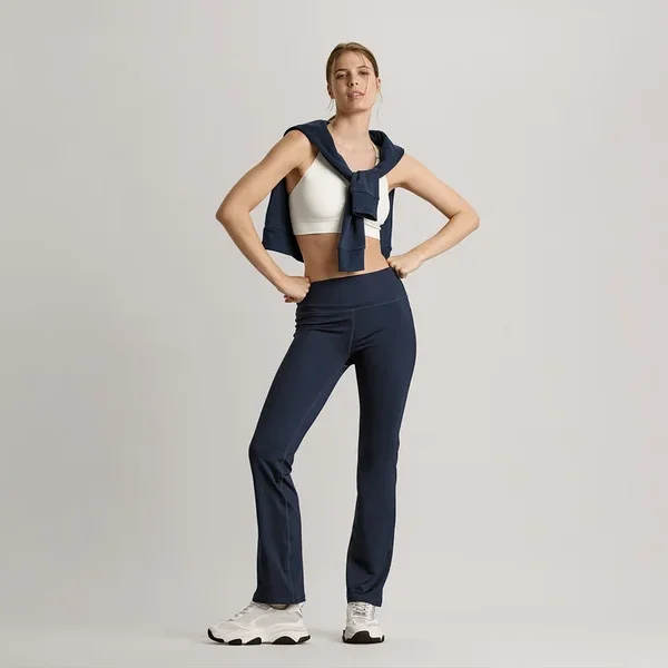 Frau posiert mit Sweatjacke in Navy um die Schultern, weißem Seamless-Sport-Bustier und marineblauer Bodyforming-Sporthose.