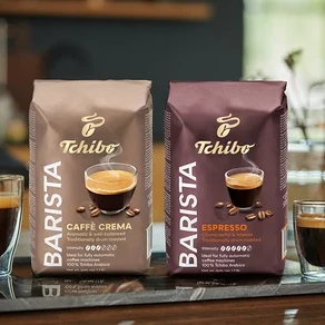 Két pohár kávé és két csomag Tchibo BARISTA Caffè Crema szemes kávé áll egy márványlapon.