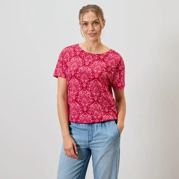 Frau trägt ein rotes, gemustertes T-Shirt und blaue Jeans.