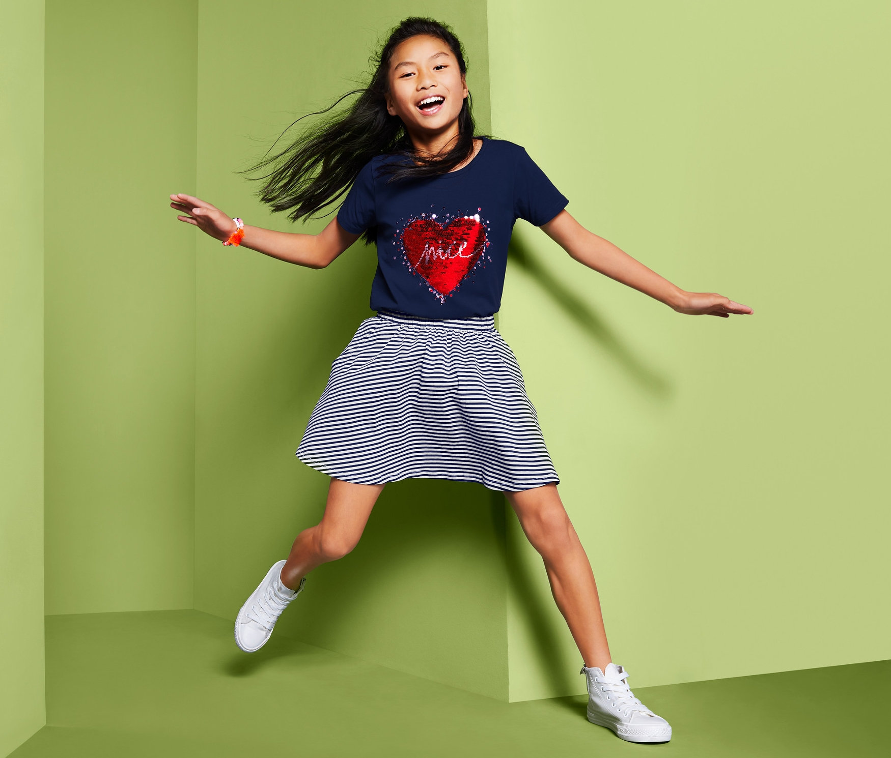 Lány ugrál világoszöld háttér előtt, szoknyát visel.