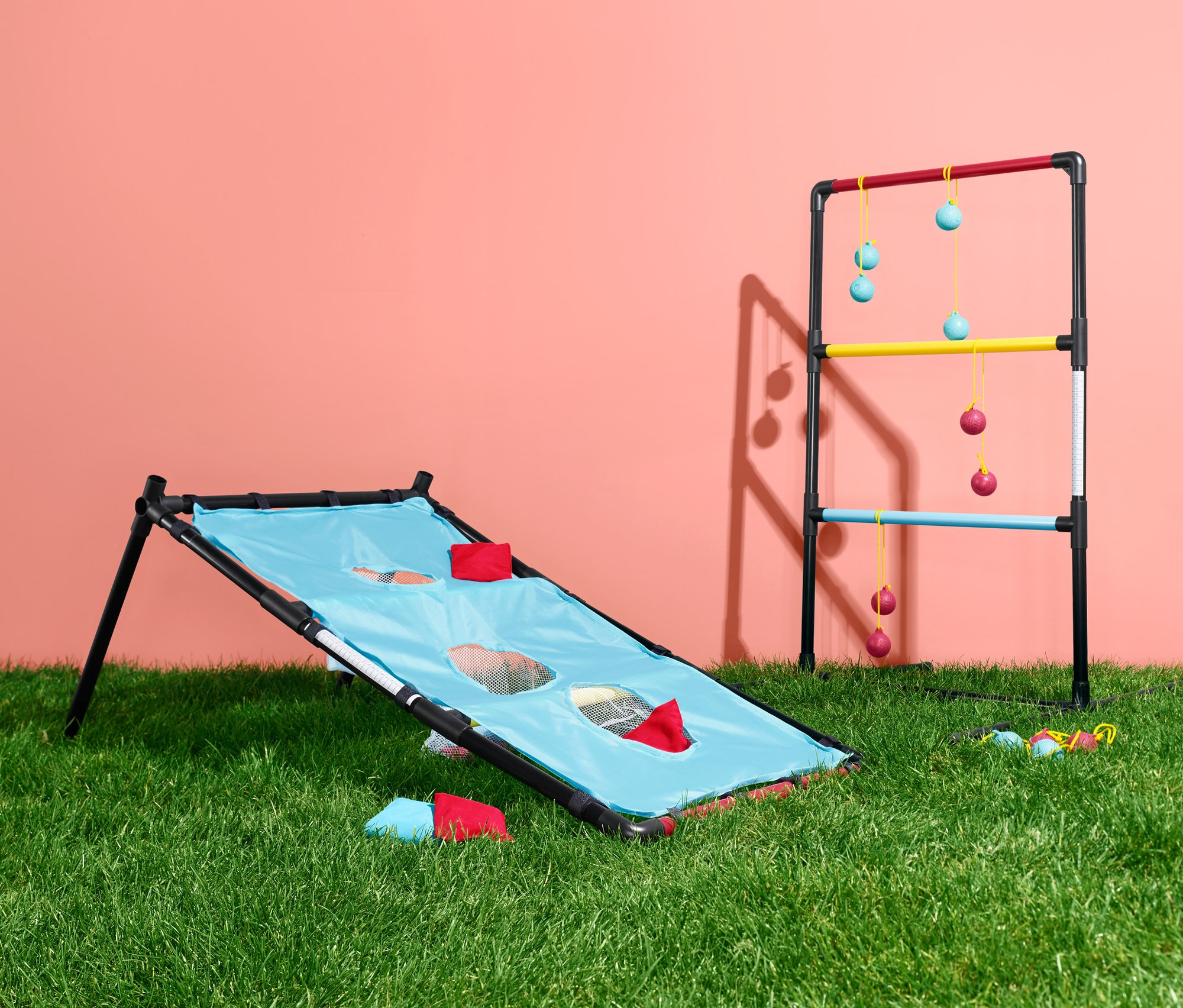 Két kültéri dobójáték a füvön. Az egyik játék kék szövetfelülettel és lyukakkal rendelkezik, a másik pedig létrával, színes fokokkal és függő labdákkal.