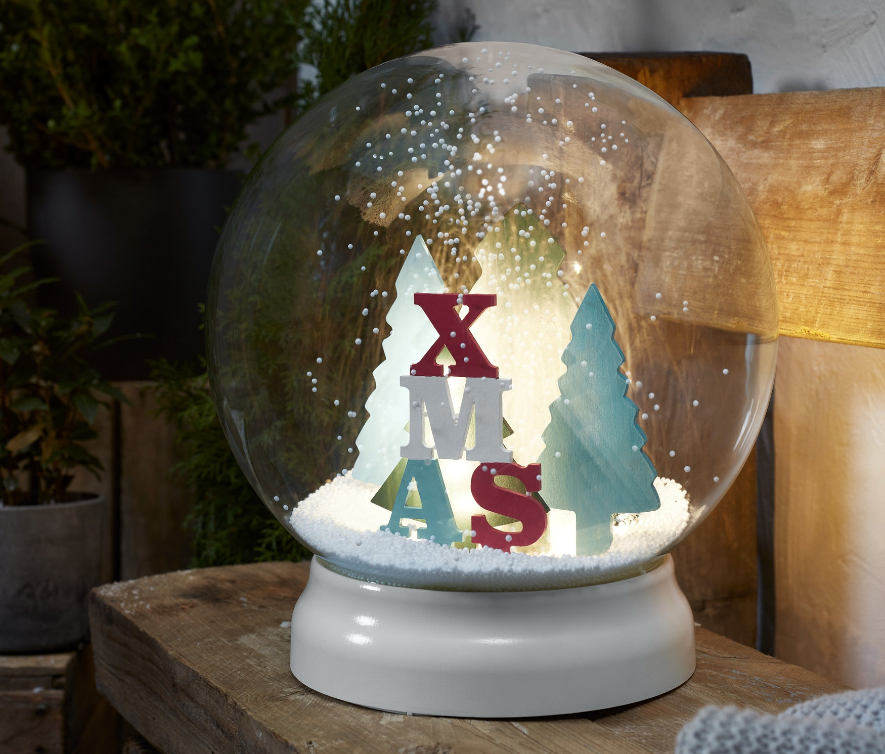 Egy LED-es kültéri hógömb XMAS felirattal és fákkal belül, fa felületen.