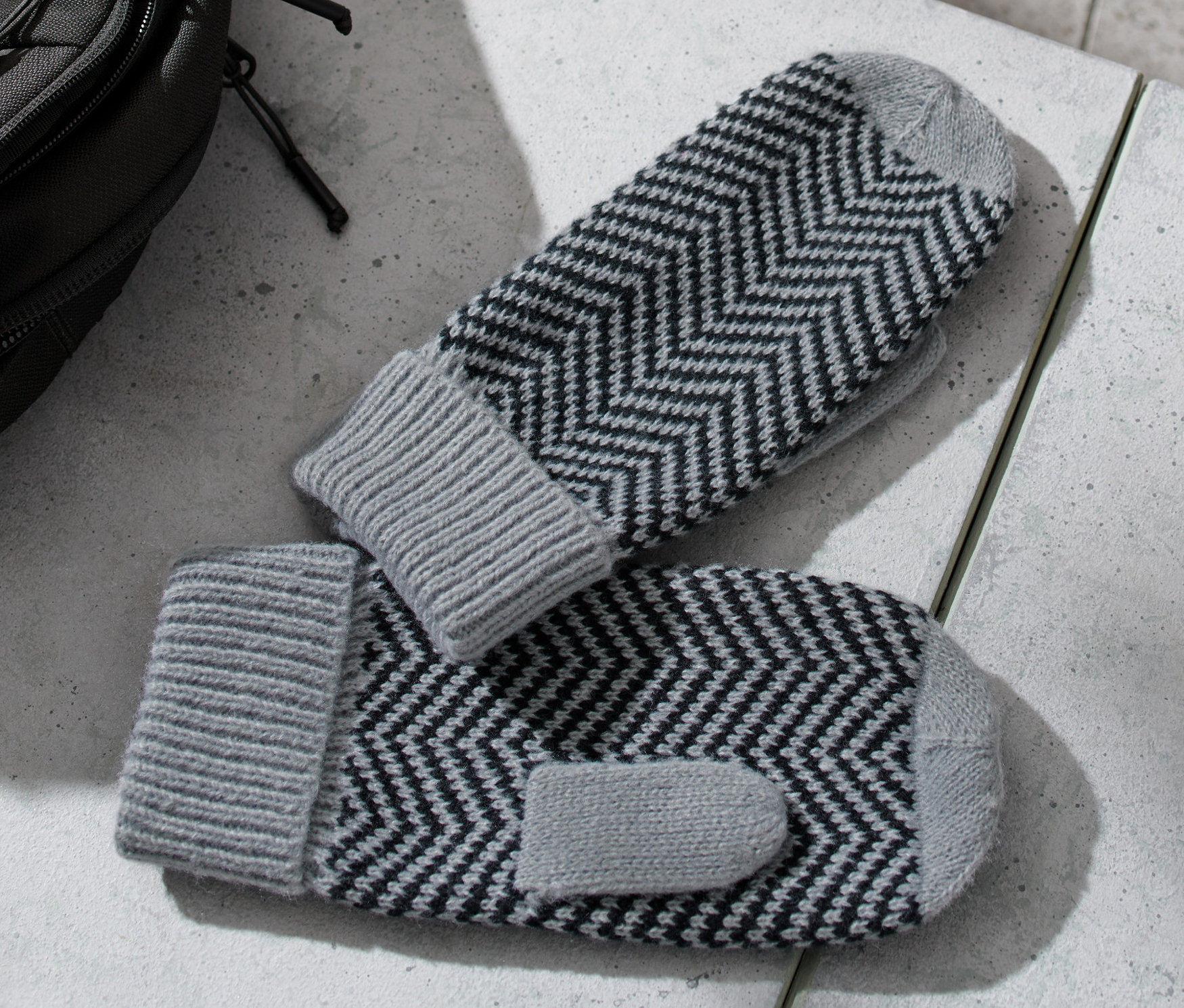 Az asztalon egyujjas kötött kesztyűk, mellette egy hátizsák és egy vizes palack.