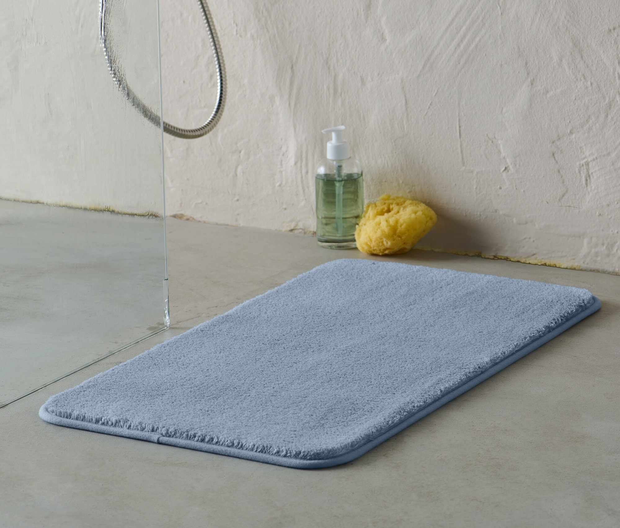 Egy kék színű, kb. 70 x 40 cm-es fürdőszobaszőnyeg a padlón, a zuhanyzó mellett.