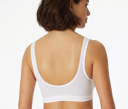 Hátulnézet egy barna hajú nőről, aki egy fehér 2 SCHIESSER kosaras bustier melltartót visel biopamuttal.