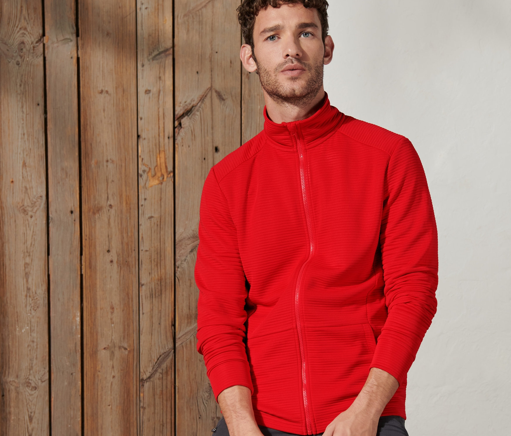 Férfi ül egy fagerendán, narancspiros funkcionális felsőt visel.