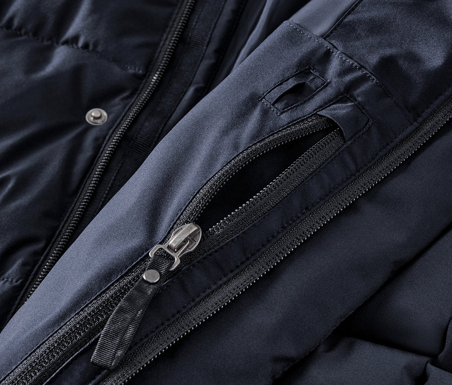 Sötétkék, steppelt parka kabát részlete, cipzárral és gombokkal.