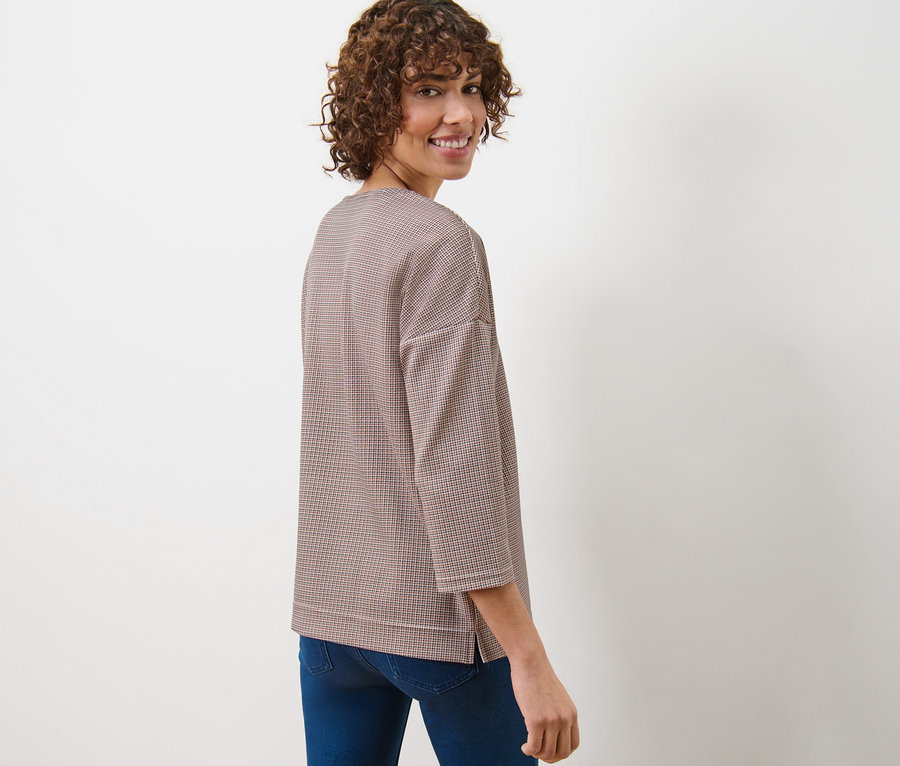 Egy nő a válla fölött hátra néz, kockás szabadidőfelsőt és farmert visel.