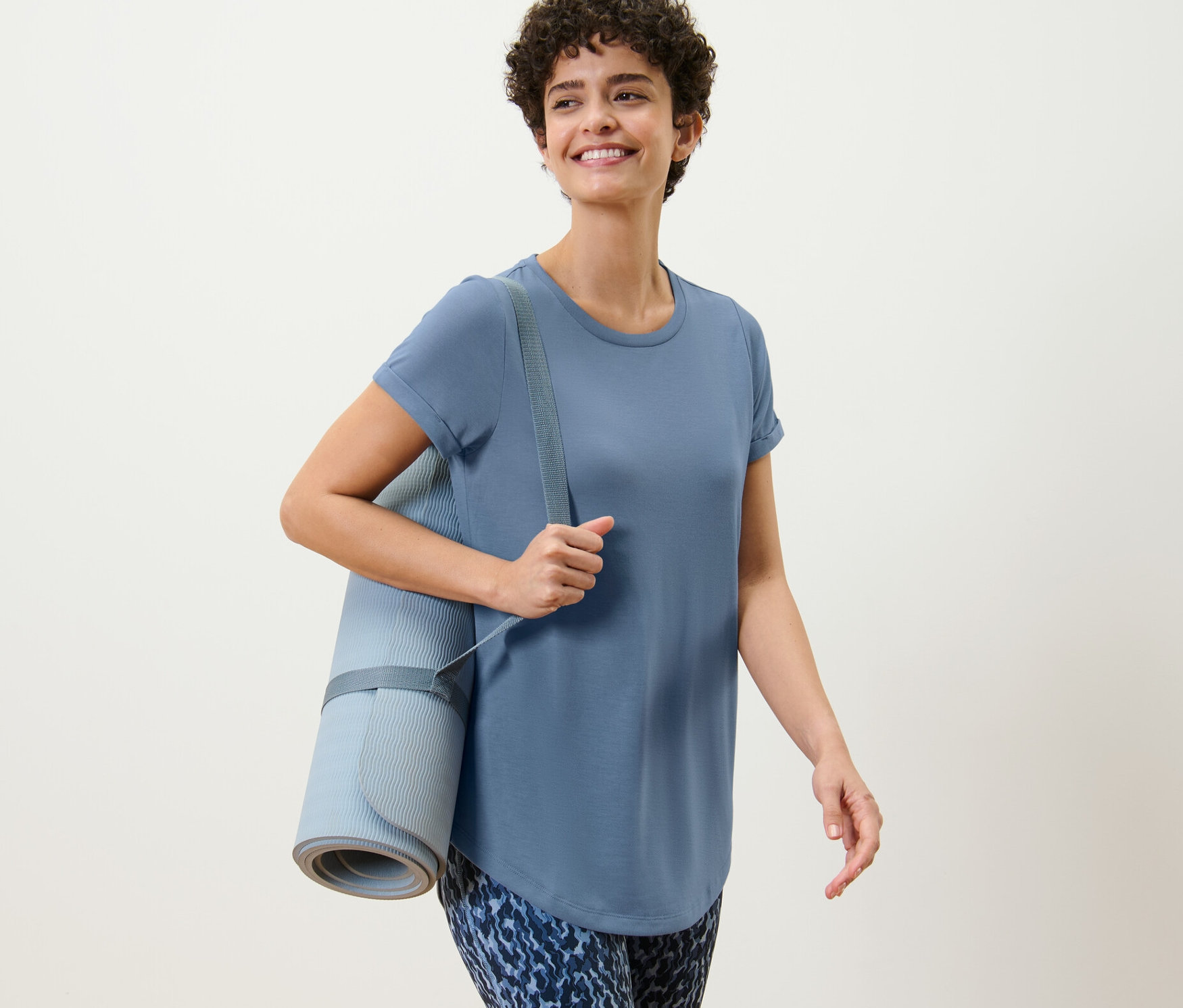 Barna hajú nő jógamatracot és egy kék női hosszú felsőt visel.
