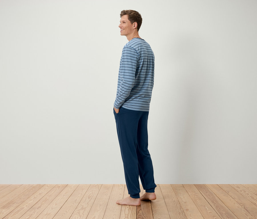 Egy férfi oldalra állva, kék csíkos hosszú ujjú inget és sötétkék nadrágot visel.