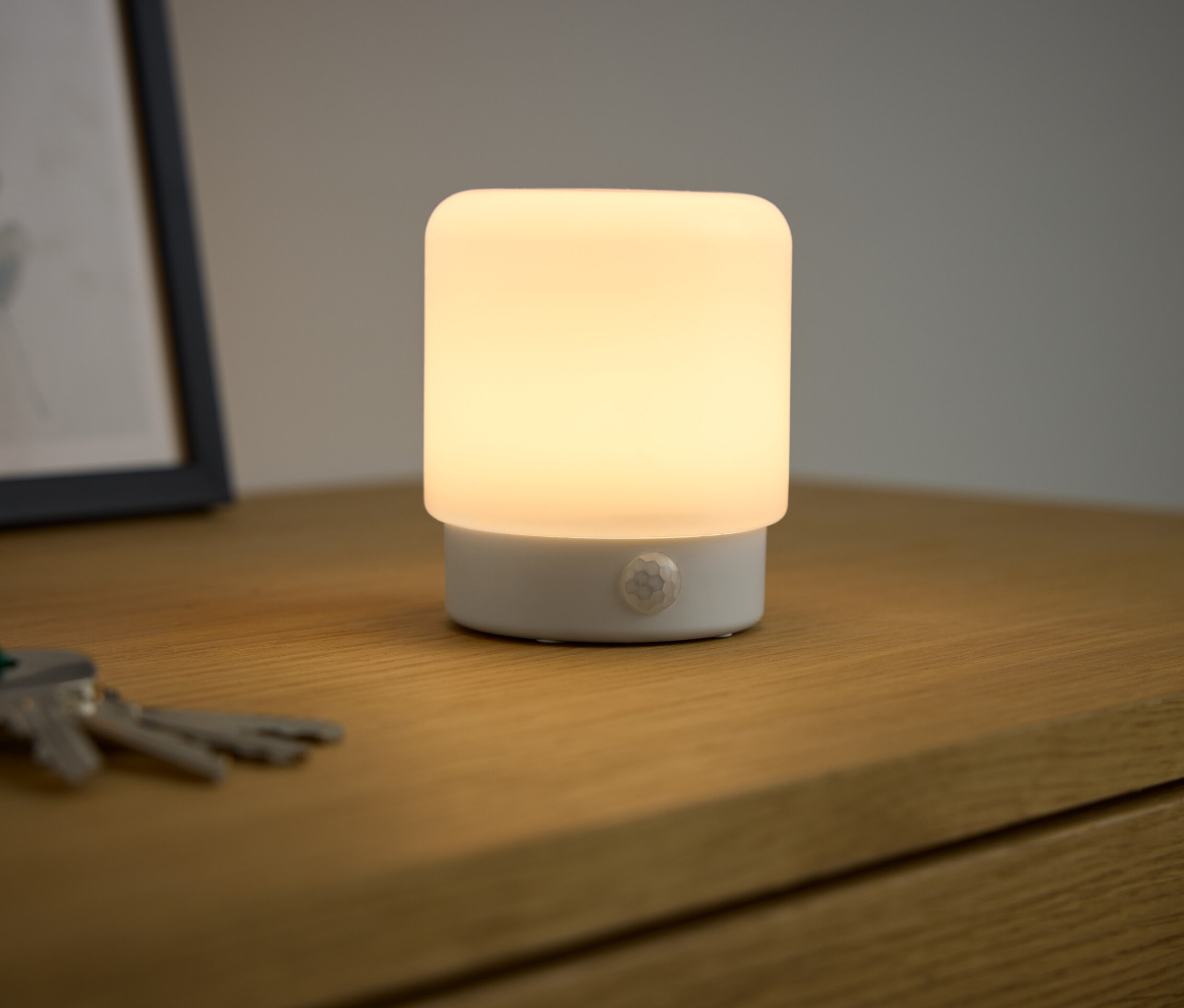 Egy LED-Mini-Multifunktionslicht mit Bewegungsmelder világít egy fa asztalon.