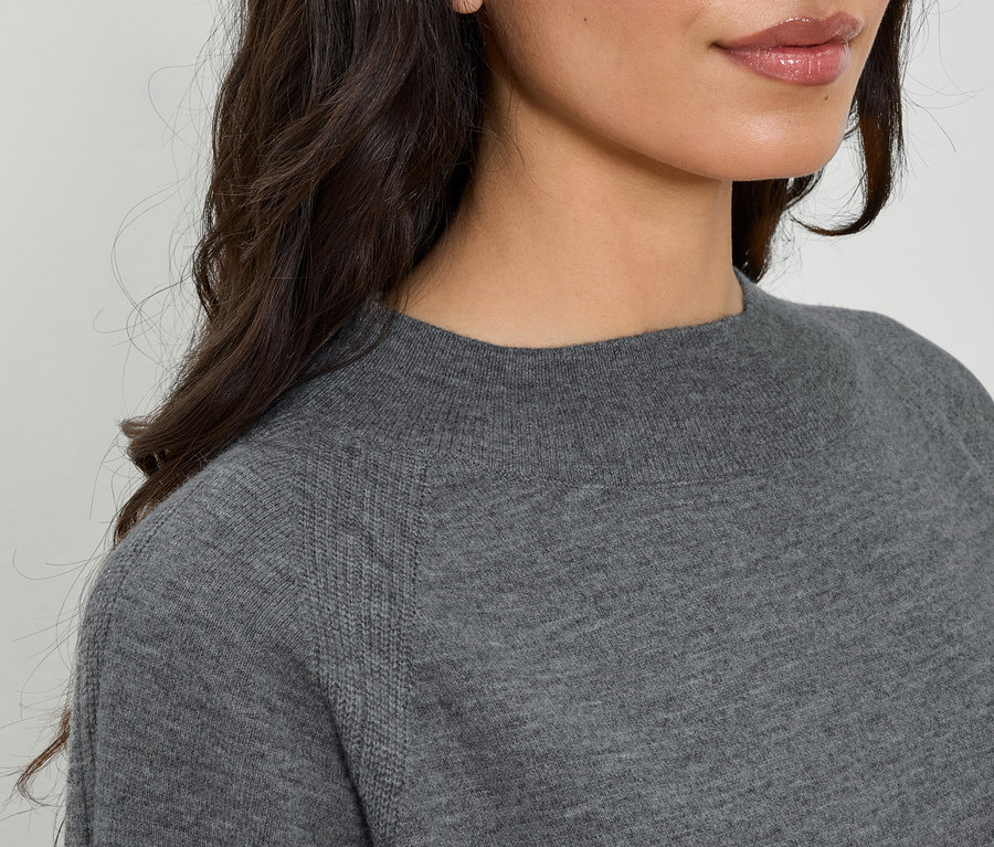 Egy nő részlete szürke, hosszú ujjú, kerek nyakú pulóverben.