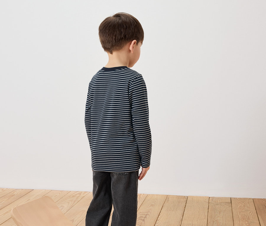 Egy fiú háttal áll a kamerának, csíkos, hosszú ujjú pólót és farmert visel.