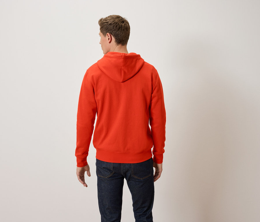 Egy férfi háttal a kamerának narancssárga kapucnis pulóvert és kék farmert visel.