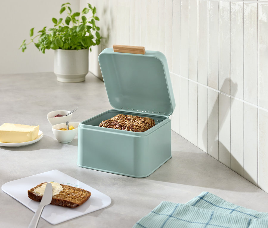 Nyitott világoskék kenyértartó doboz kenyérrel, mellette vaj, lekvár, kés és megkent kenyér.