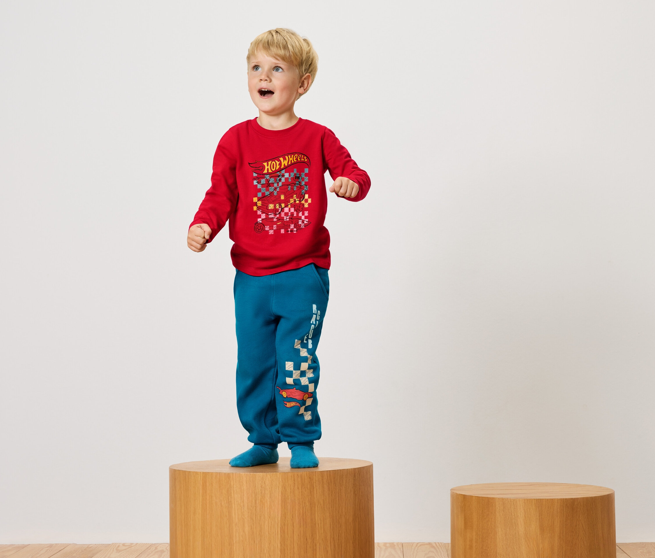 Fiú áll egy faemelvényen piros pólóban és kék nadrágban.
