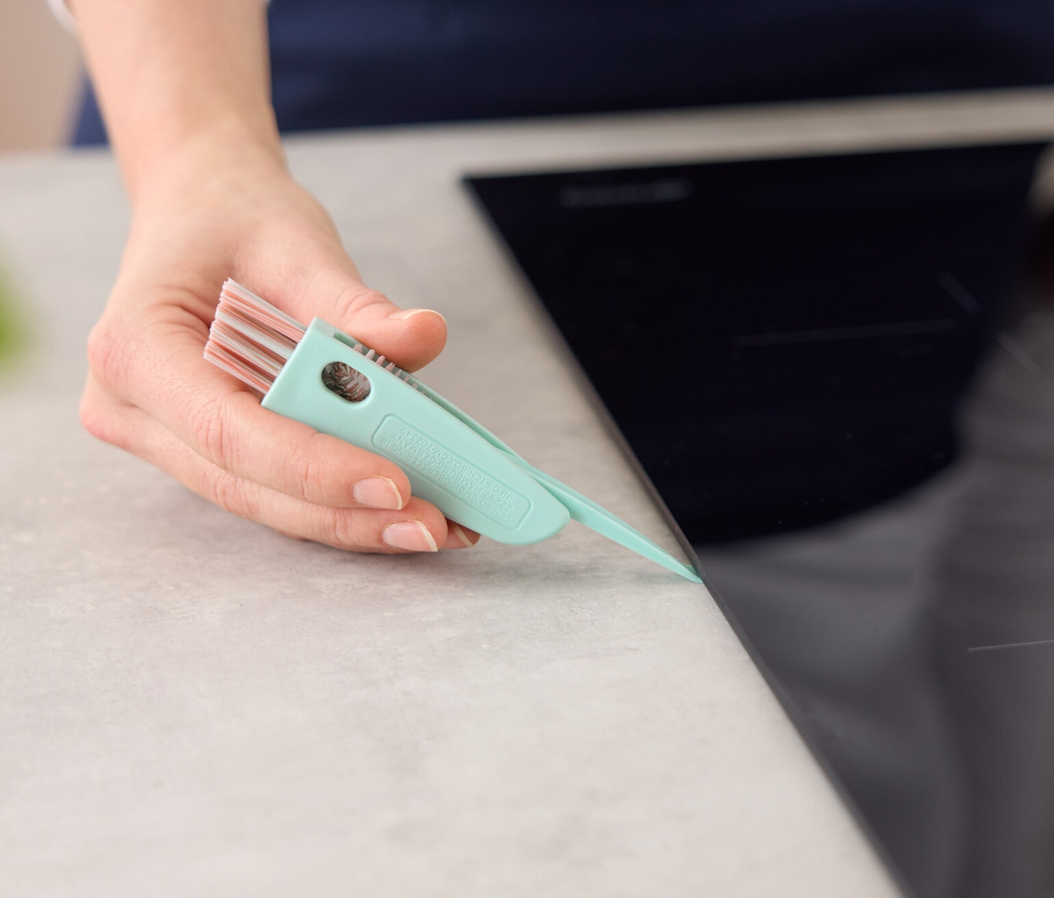 Nő tisztítja a főzőlap szélét egy 3 az 1-ben tisztítókefével.