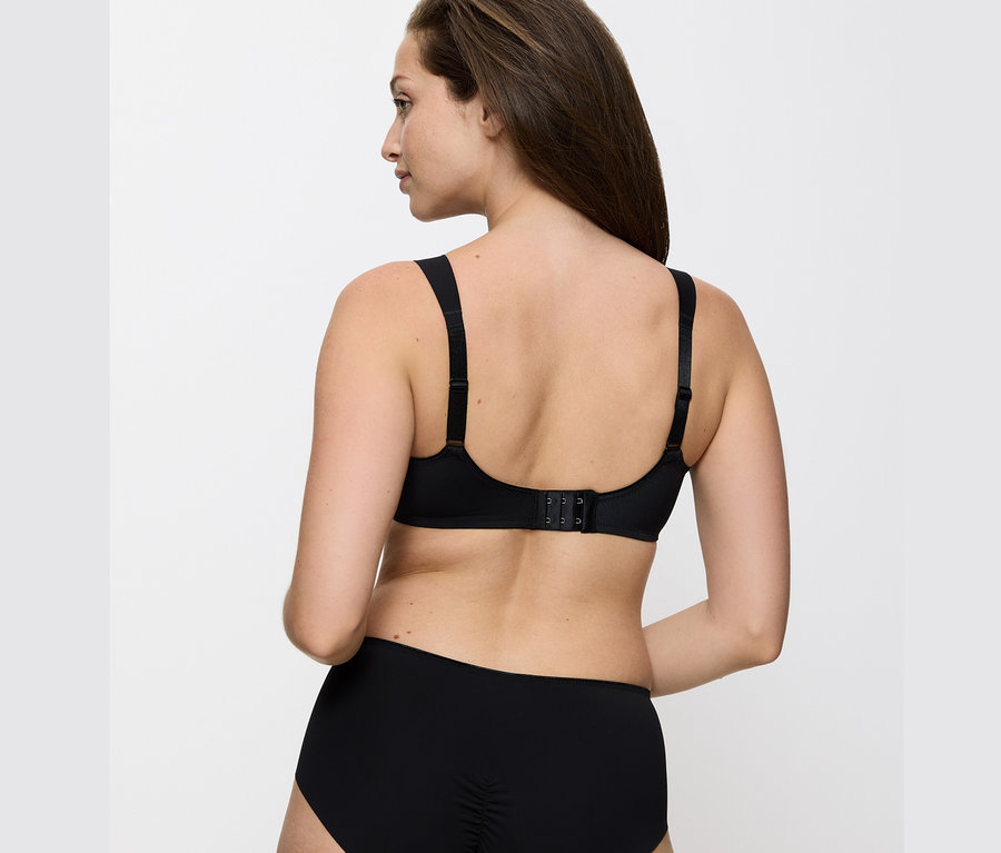 Hátsó nézet egy barna hajú nőről, aki fekete Triumph Essential »Minimizer W X« melltartót és fekete alsóneműt visel.