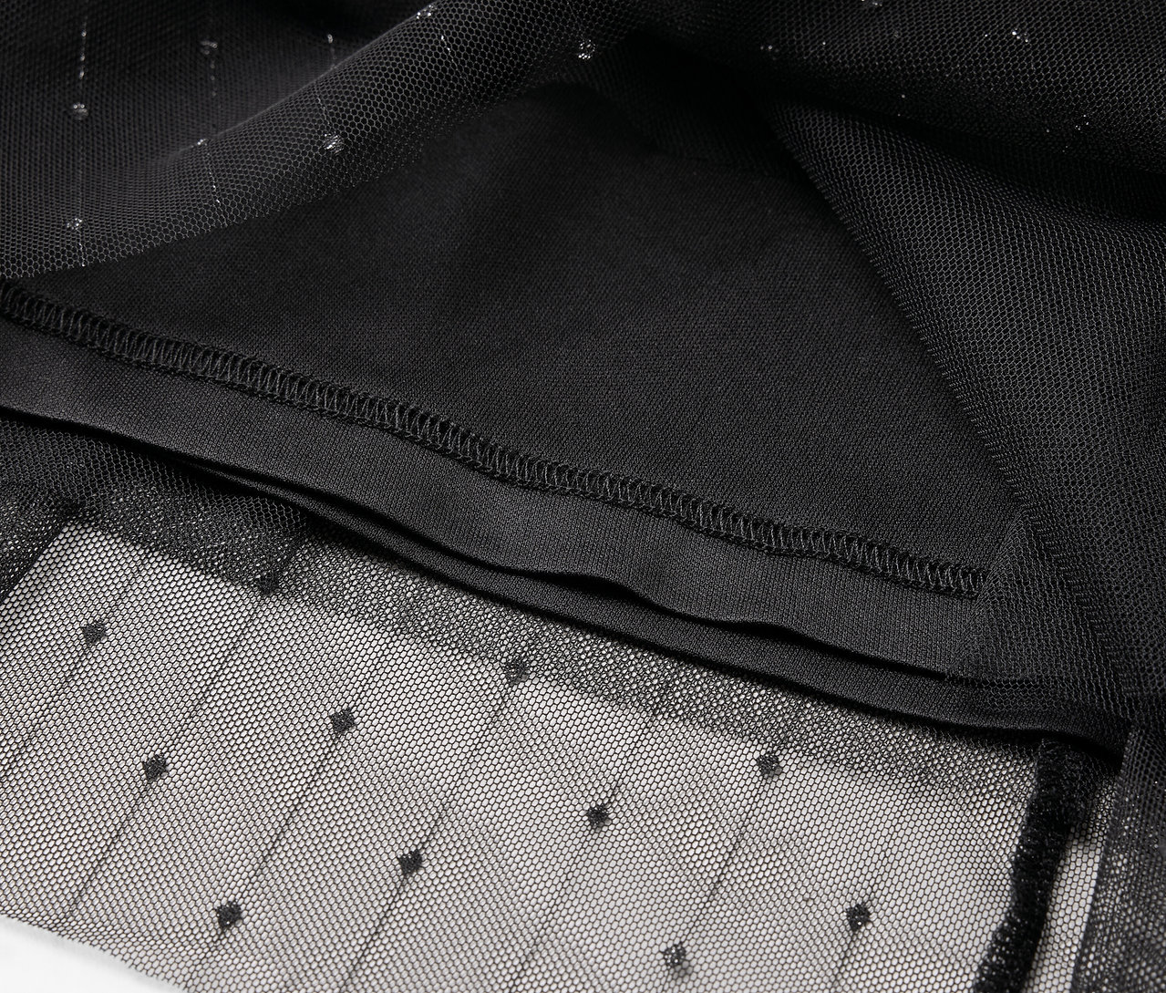 Egy fekete tüll ruhadarab részlete pöttyös mintával és belső béléssel.