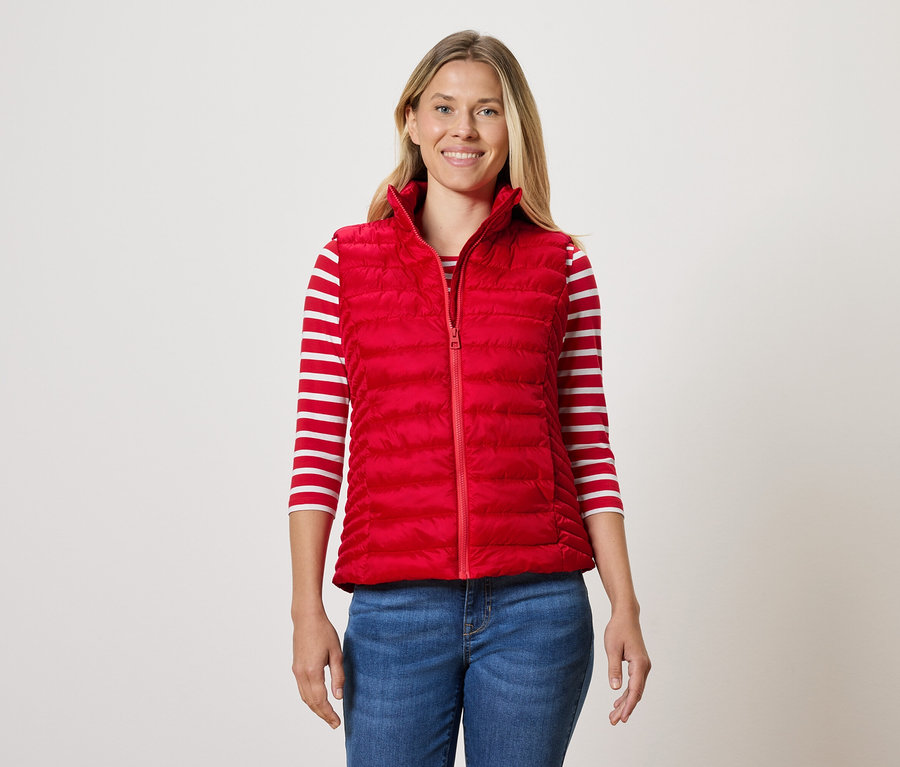 Nő visel piros steppelt mellényt, csíkos pólót és farmert.