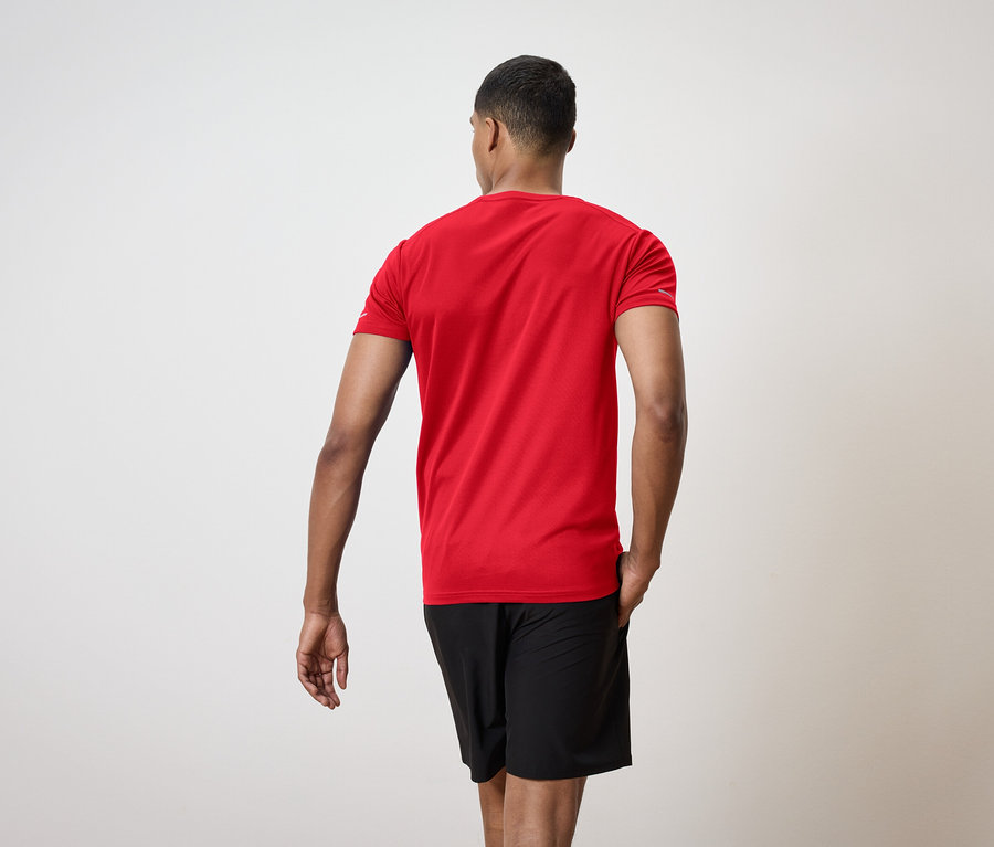 Egy férfi háttal a kamerának, piros pólót és fekete rövidnadrágot visel.