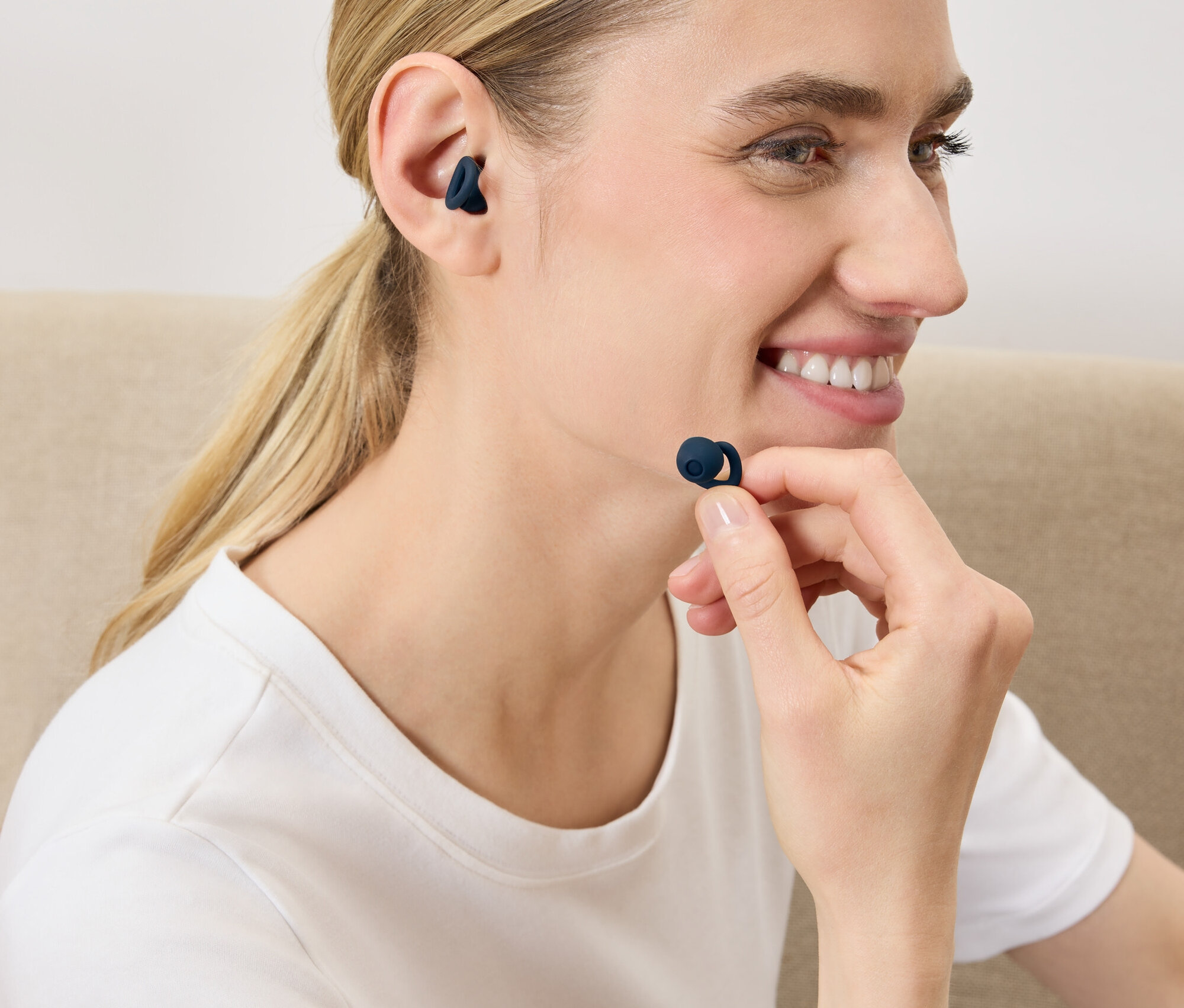 Egy nő sötétkék vezeték nélküli fülhallgatót helyez a fülébe.