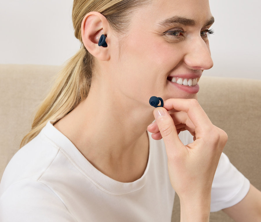 Egy nő sötétkék vezeték nélküli fülhallgatót helyez a fülébe.