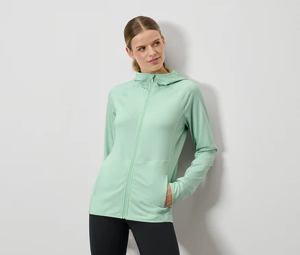 Nő pózol mentazöld kapucnis pulóverben és fekete leggingsben.
