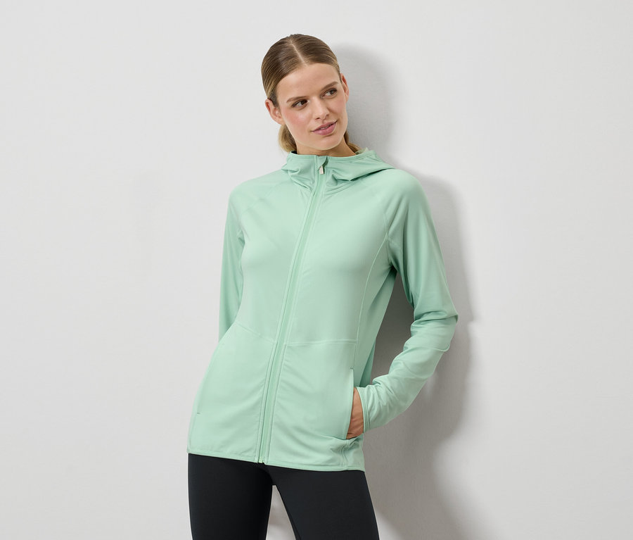 Nő pózol mentazöld kapucnis pulóverben és fekete leggingsben.