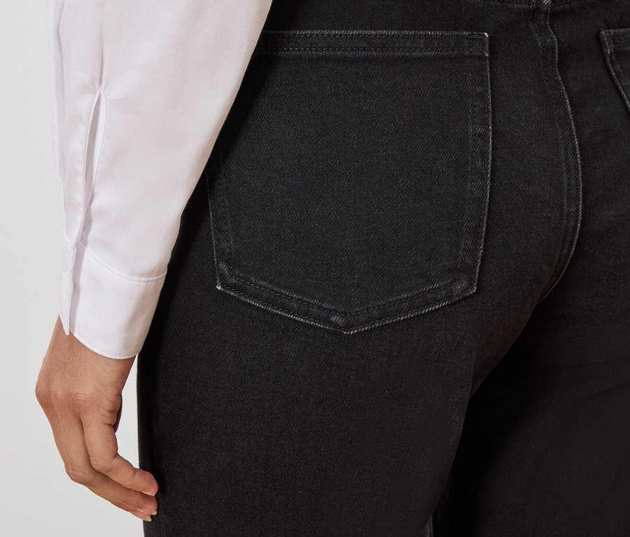 Fekete farmernadrág hátsó részletének közeli képe egy fehér inget viselő személyen.