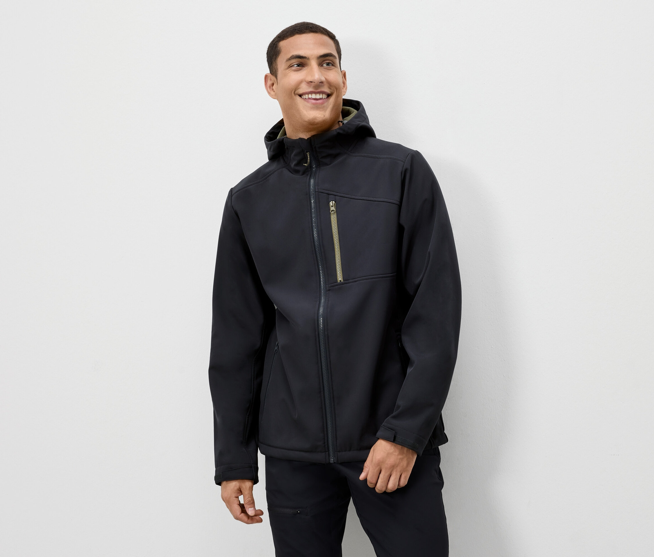 Egy férfi mosolyog, és fekete kapucnis kabátot visel.