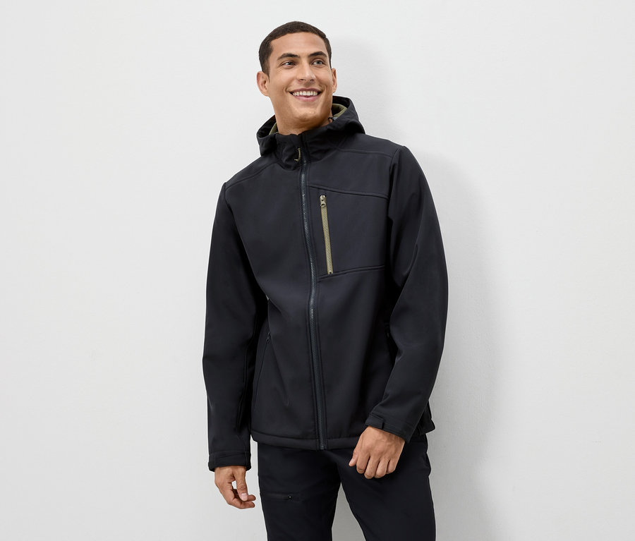 Egy férfi mosolyog, és fekete kapucnis kabátot visel.