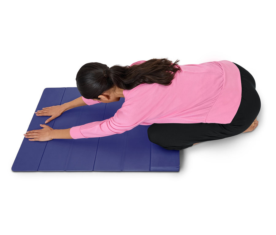 Nő rózsaszín felsőben és fekete nadrágban nyújtózik egy kék szőnyegen.