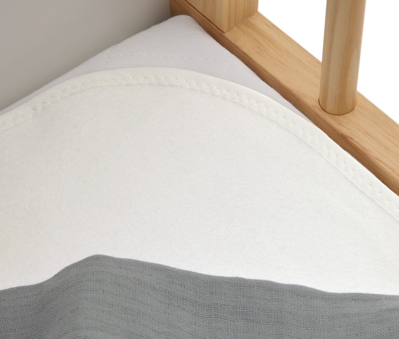 Egy fehér matrac közeli képe szürke ruhával egy fa ágyon.