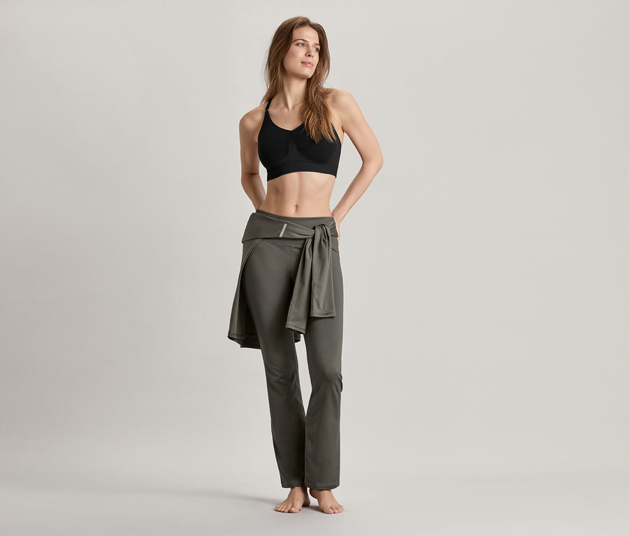 Nő visel varrásmentes bustier sportmelltartót, fekete és alakformáló sportnadrágot, olívazöld.