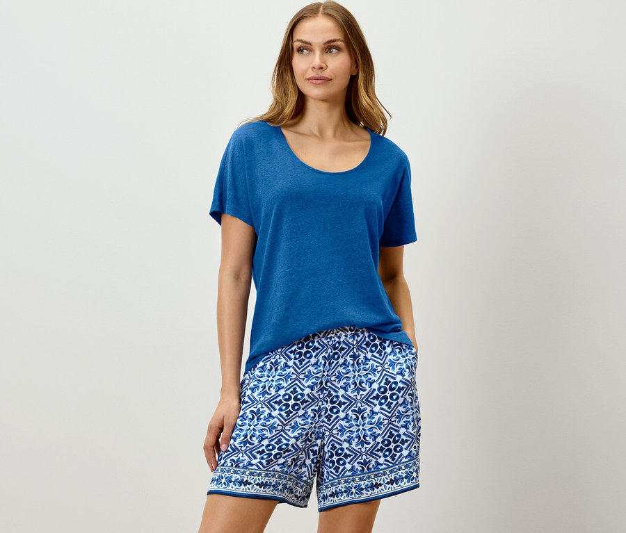 Nő visel kobaltkék lenvászon pólót és kék mintás rövidnadrágot.