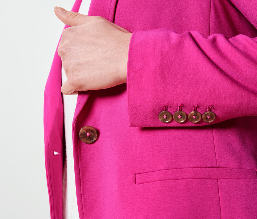Közelkép egy rózsaszín blézerről, barna gombokkal az ujjakon és a záródáson.