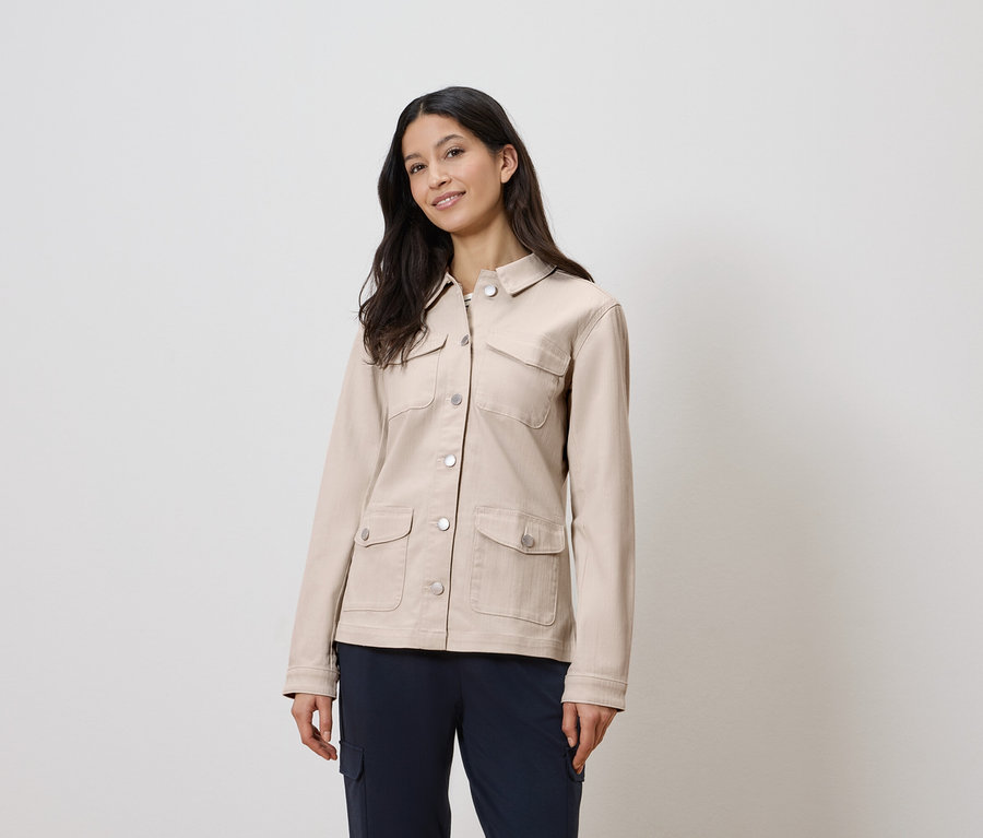 Nő visel egy bézs kabátot és kék nadrágot.