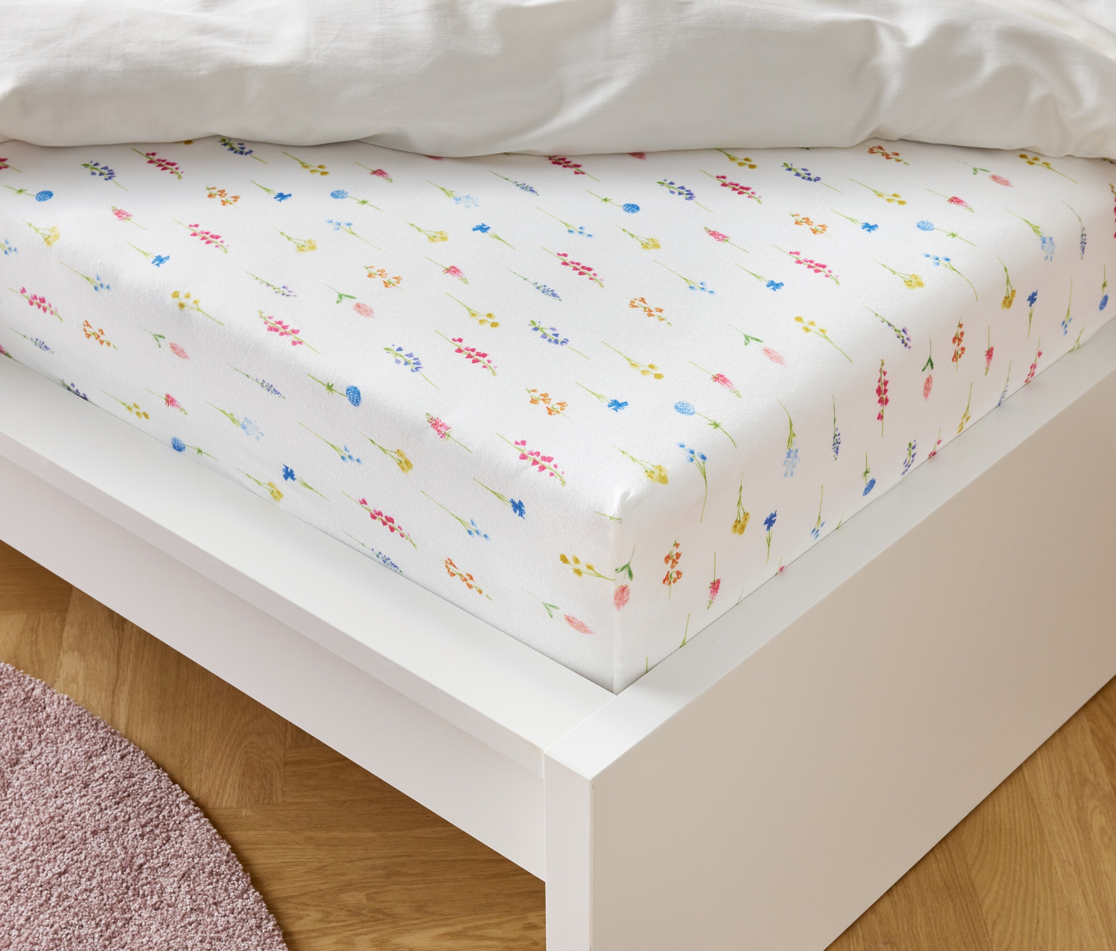 Egy virágmintás fehér gumis lepedő fekszik egy fehér ágykereten.