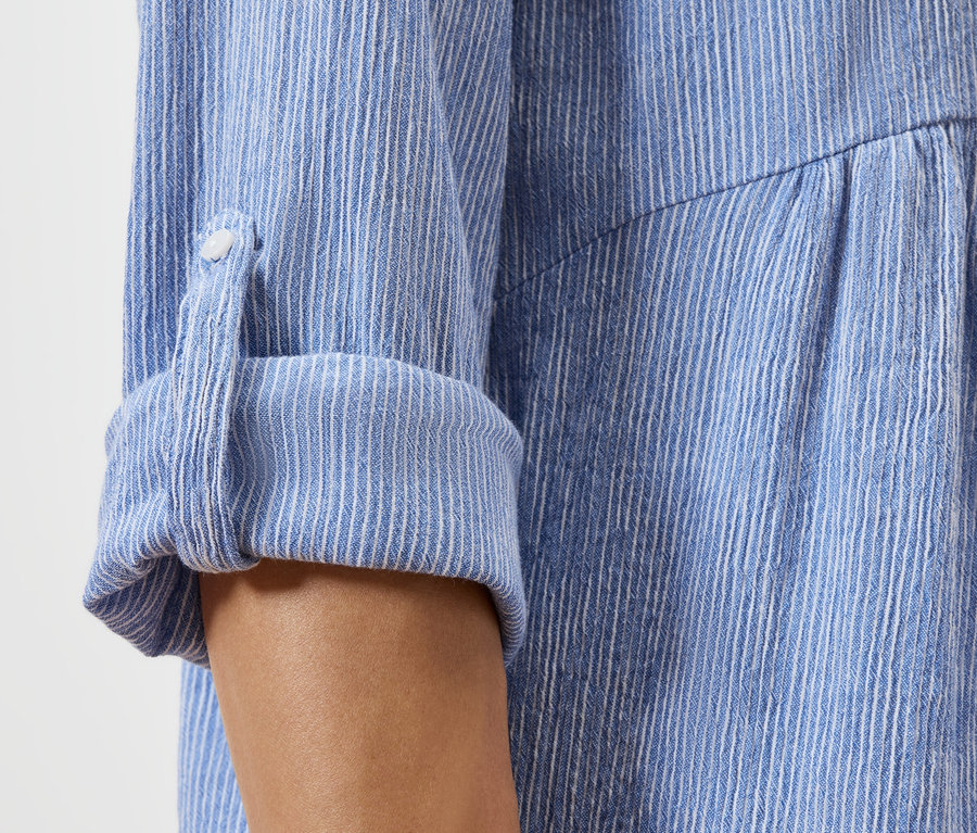 Kék-fehér csíkos ing felgyűrt ujjának közelképe.