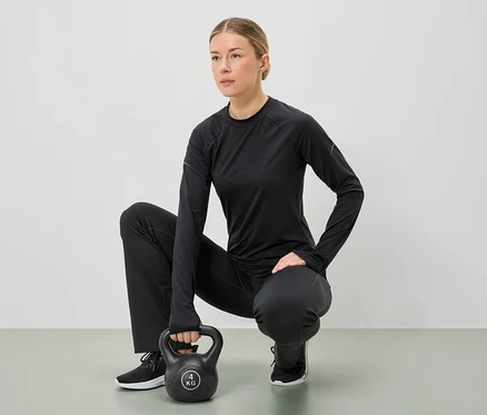 Fekete sportruházatot viselő nő guggol, és mindkét kezével egy 4 kg-os kettlebellt tart.