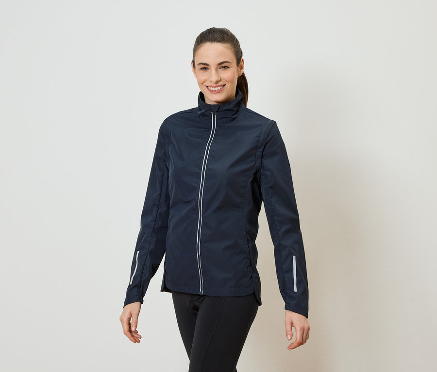 Egy lófarokos nő tengerészkék, cipzáros kabátot és fekete leggingset visel.