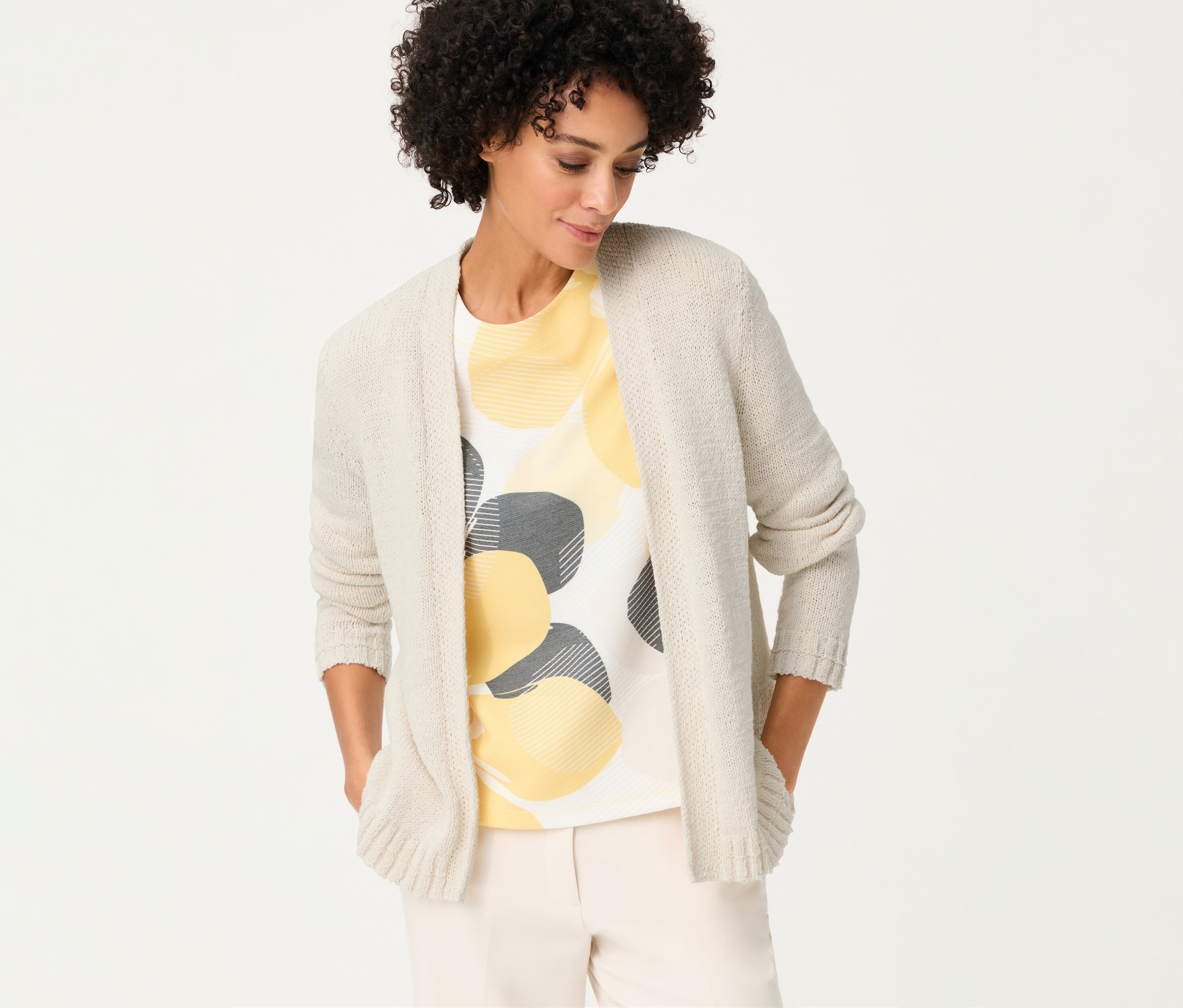 Nő Olsen lenvászon kardigánban, sárga és szürke körökkel díszített pólóval, kezét a zsebébe dugva.