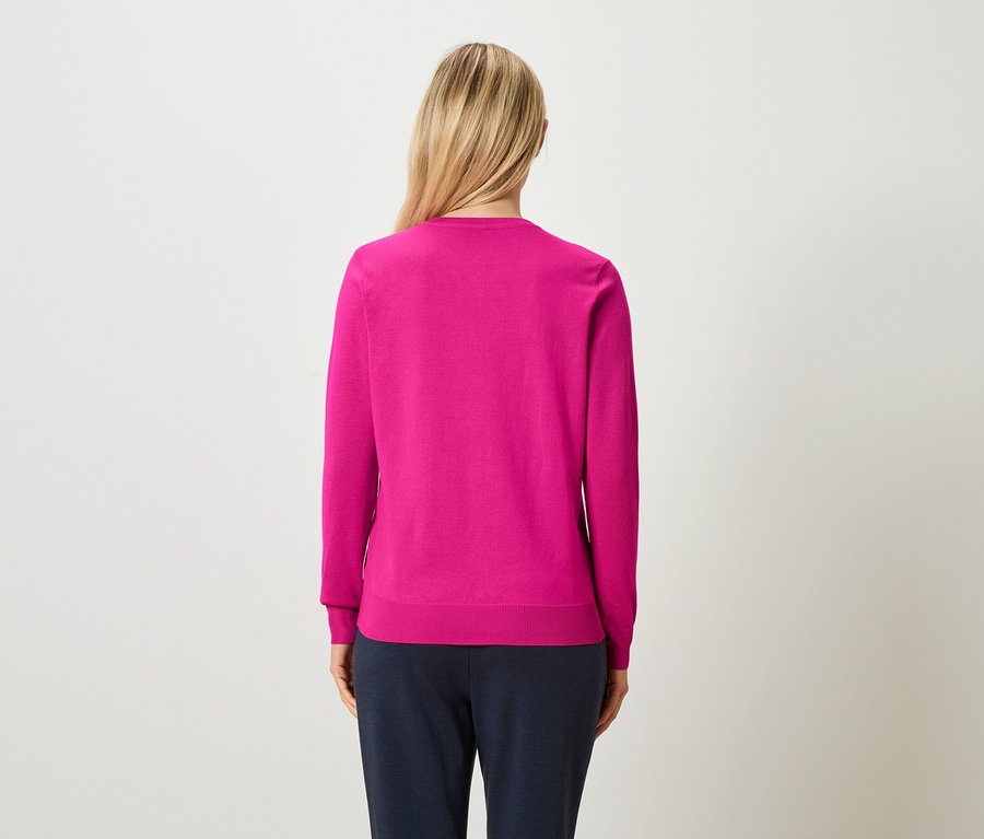 Hátulról látható egy szőke, feltűzött hajú nő, aki rózsaszín pulóvert és sötétkék nadrágot visel.