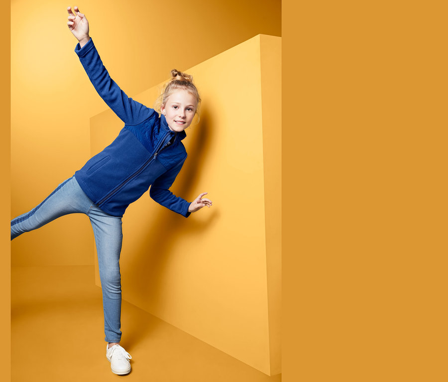 Lány pózol egy lány mikropolár felsőben sárga háttér előtt.